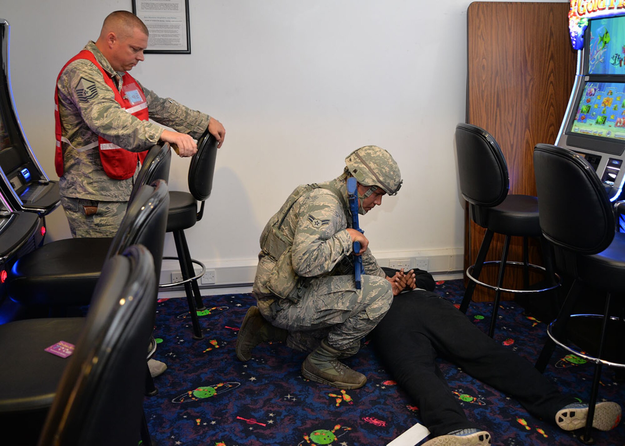 A member of the 100th Air Refueling Wing inspection team evaluates the situation as a U.S. Air Force 100th Security Forces Squadron Airman handcuffs a simulated active shooter during an exercise at the bowling alley Aug. 17, 2017, on RAF Mildenhall, England. The wing inspection team includes subject matter experts from a wide variety of agencies around base, who provide input into the exercise and monitor each scenario. (U.S. Air Force photo by Karen Abeyasekere)