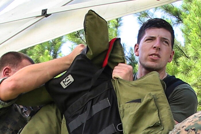 A Marine slips into an explosive ordnance disposal suit with the help of a fellow Marine.
