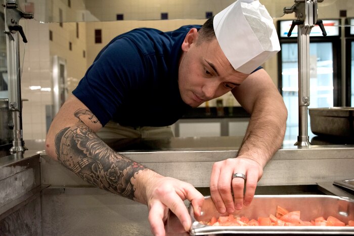 A soldier prepares food in a commercial kitchen.