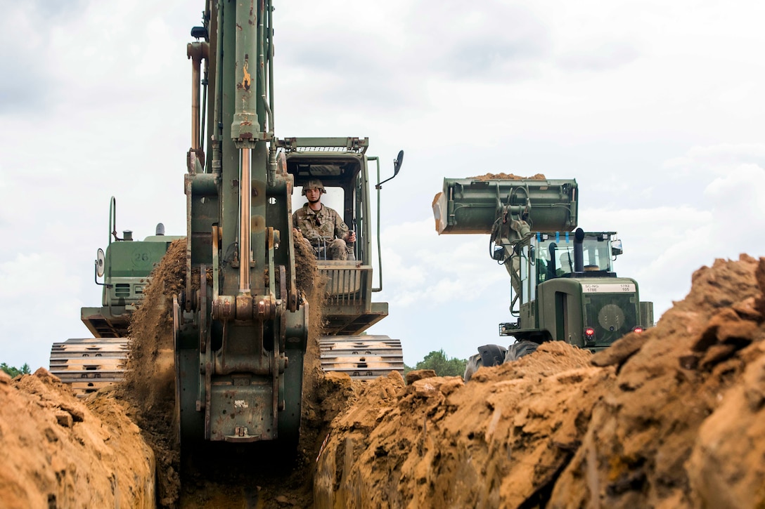 A soldier operates a heavy equipment excavator.