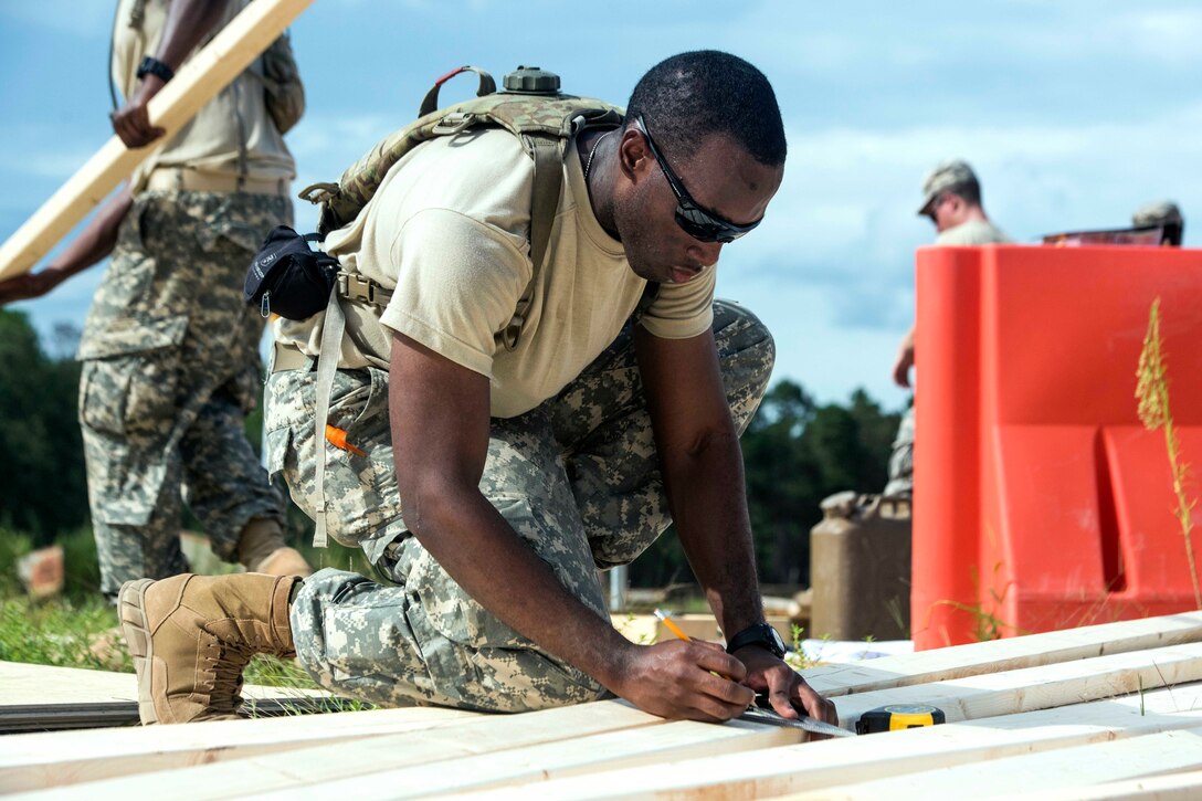 Army Pvt. Romaio Whittaker uses a framing square to mark lumber.