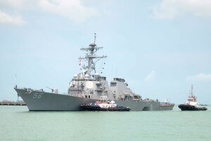 A tug boat pushes a guided-missile destroyer.