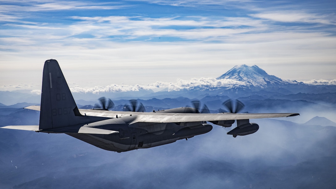 An aircraft flies near a snow-capped mountain.