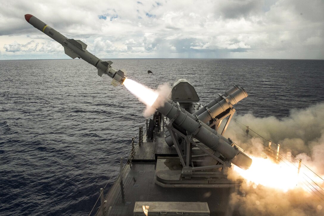 A missile launches over the sea from a ship's deck.