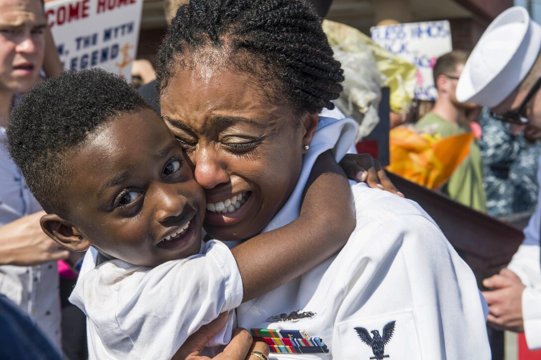 A sailor tearfully hugs a boy amid a crowd of people.