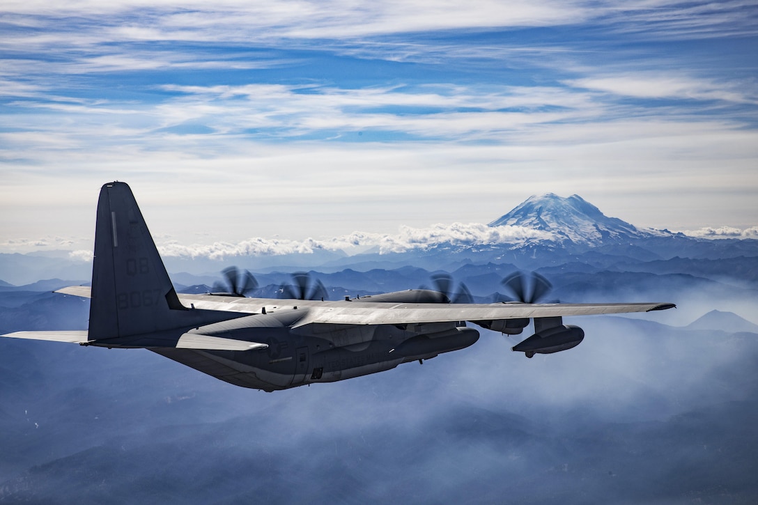 An aircraft flies near a snow-capped mountain.