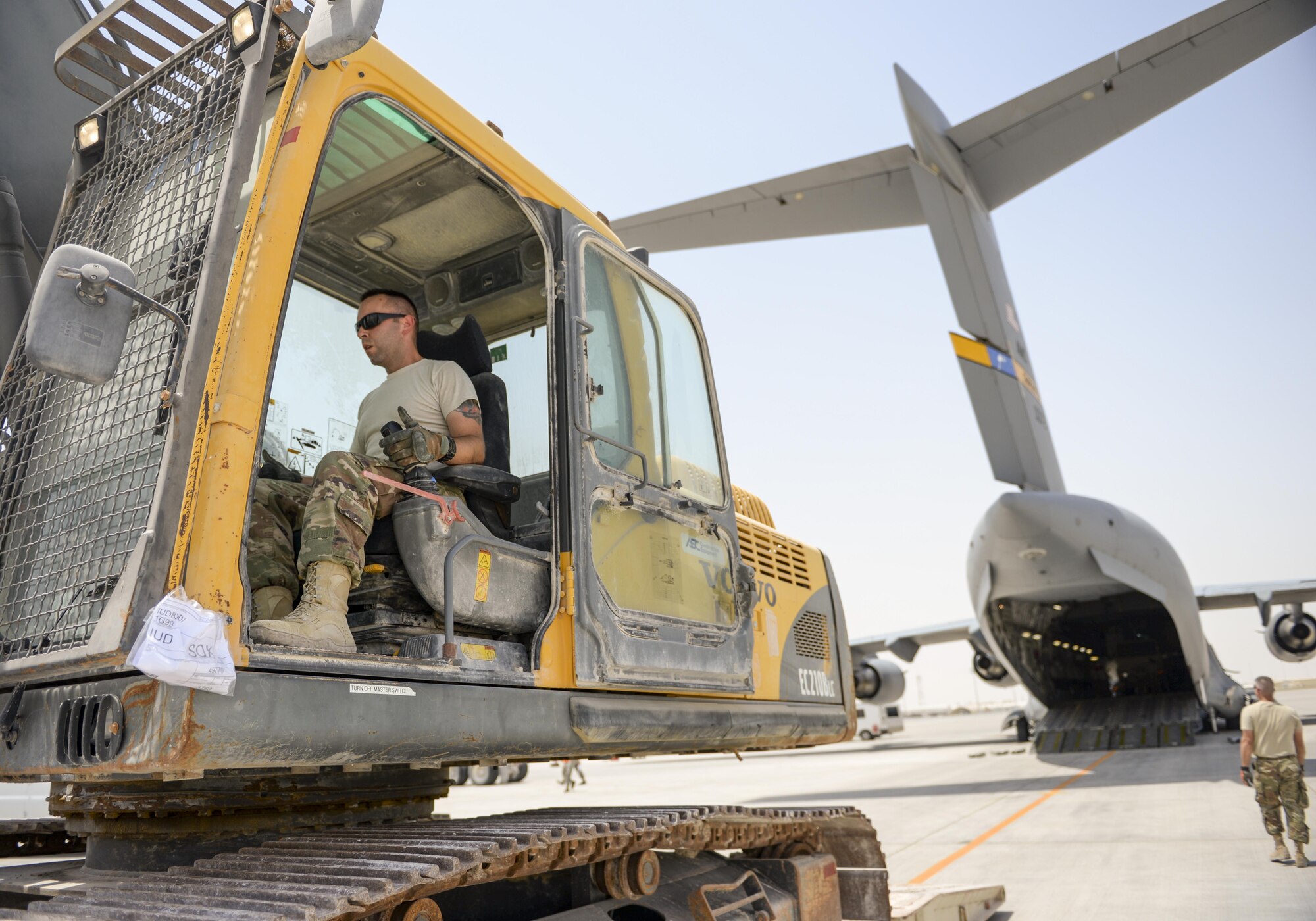 U.S. Air Force Staff Sgt. David Wakeman, airfield operator assigned to the 557th Expeditionary RED HORSE Squadron, unloads an excavator from a low-boy trailer before loading the equipment into a C-17 Globemaster III at Al Udeid Air Base, Qatar, Aug. 7, 2017.