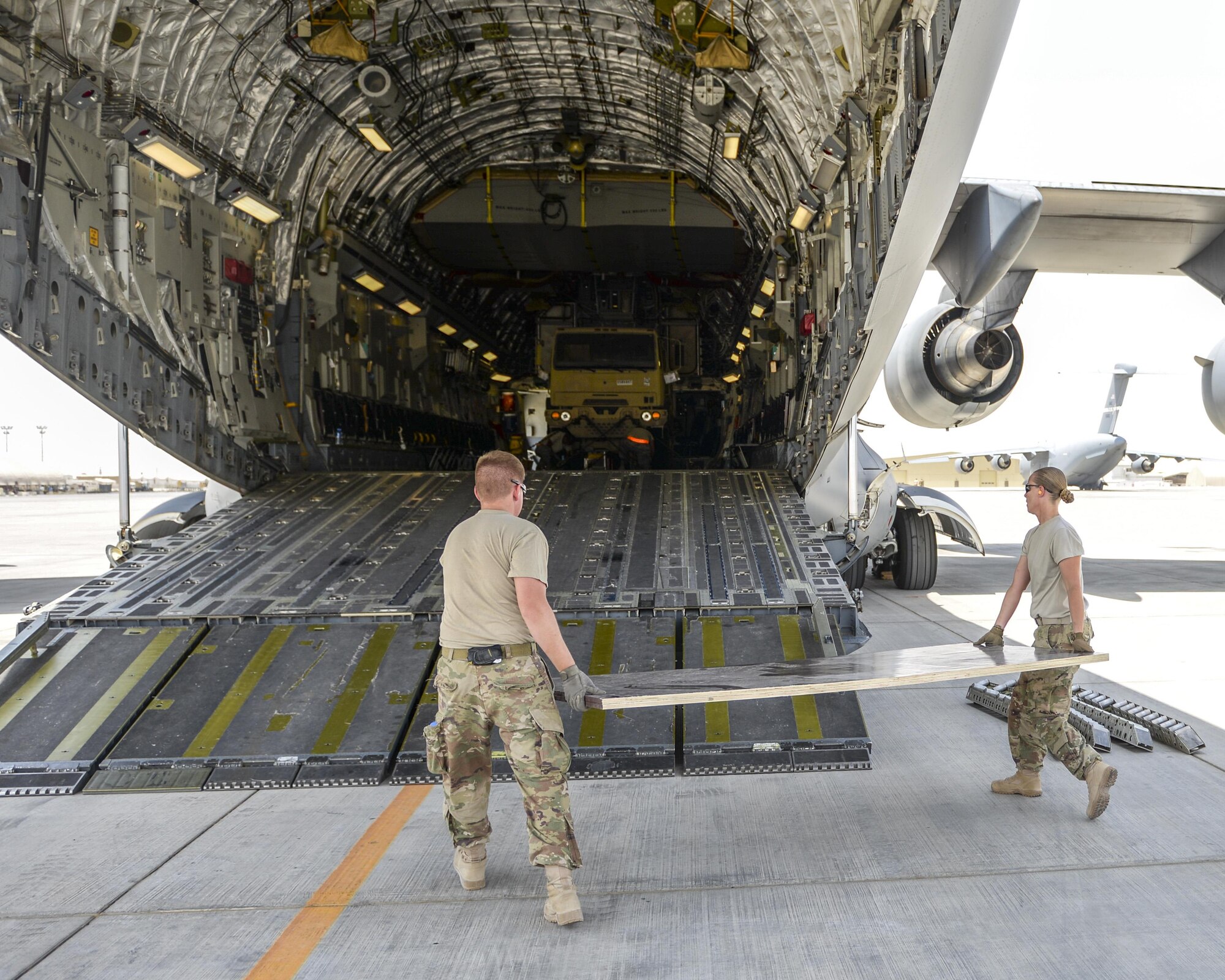 U.S. Air Force Staff Sgt. Leigh Sullivan, right, and Senior Airman Jonathan Moore, members of the cargo movement team assigned to the 557th Expeditionary RED HORSE Squadron lay plywood to protect a C-17 Globemaster III prior to loading an excavator onto the aircraft at Al Udeid Air Base, Qatar, Aug. 7, 2017.