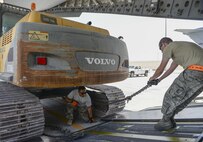 U.S. Air Force Technical Sgt. Alexander Nunez, on the ground, air transportation/cargo movement team non-commissioned officer in charge assigned to the 557th Expeditionary RED HORSE Squadron, and Senior Airman Jace Fore, standing, air transportation craftsman assigned to the 8th Expeditionary Air Mobility Squadron, attach a winch system to an excavator prior to loading it onto a C-17 Globemaster III at Al Udeid Air Base, Qatar, Aug. 7, 2017. The 557th ERHS worked alongside the 8th EAMS to load the 50,000 pound excavator into a C-17 Globemaster III aircraft for transportation to an undisclosed location in the U.S. Central Command Area of Responsibility. (U.S. Air National Guard photo by Tech. Sgt. Bradly A. Schneider/Released)
