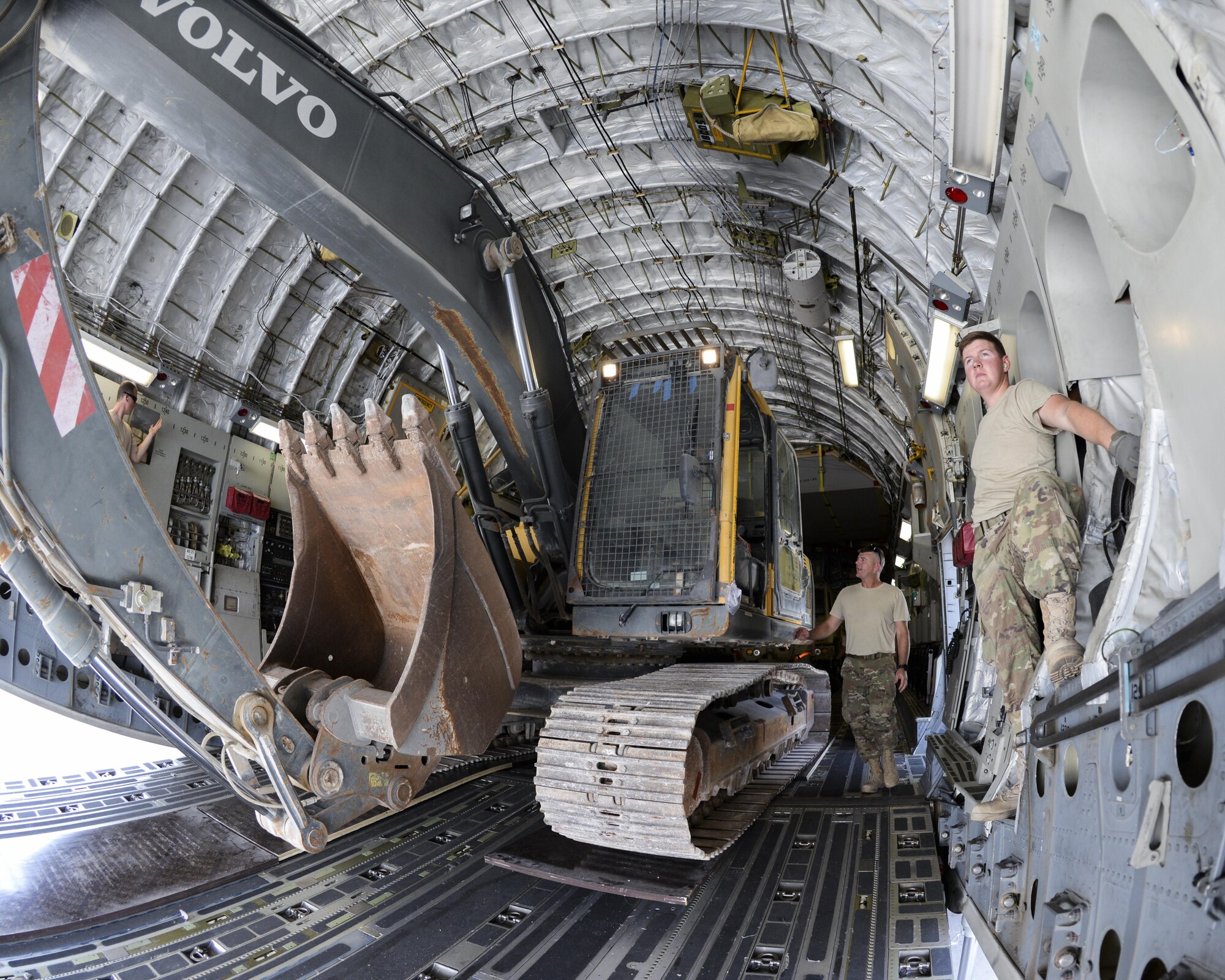 557th Expeditionary RED HORSE Squadron members, U.S. Air Force Senior Airman Jonathan Moore, far right, cargo movement team member, and Master Sgt. Ricky Johnson, standing next to the excavator, watch closely as Staff Sgt. David Wakeman, airfield operator, operates the backhoe while loading it into a C-17 Globemaster III at Al Udeid Air Base, Qatar, Aug. 7, 2017.
