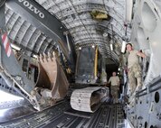 557th Expeditionary RED HORSE Squadron members, U.S. Air Force Senior Airman Jonathan Moore, far right, cargo movement team member, and Master Sgt. Ricky Johnson, standing next to the excavator, watch closely as Staff Sgt. David Wakeman, airfield operator, operates the backhoe while loading it into a C-17 Globemaster III at Al Udeid Air Base, Qatar, Aug. 7, 2017. The 557th ERHS loaded the 50,000 pound excavator into a C-17 Globemaster III aircraft for transportation to an undisclosed location in the U.S. Central Command Area of Responsibility. (U.S. Air National Guard photo by Tech. Sgt. Bradly A. Schneider/Released)