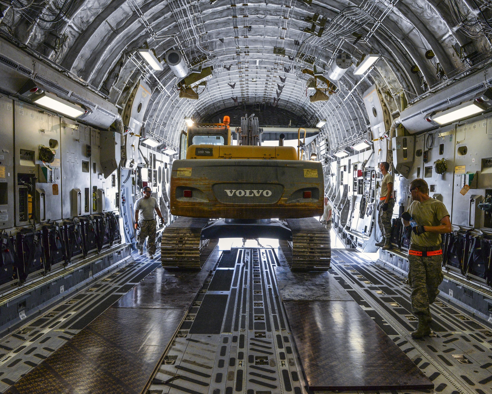 Airmen assigned to the 557th Expeditionary RED HORSE Squadron and the 8th Expeditionary Air Mobility Squadron guide an excavator into a C-17 Globemaster III at Al Udeid Air Base, Qatar, Aug. 7, 2017.