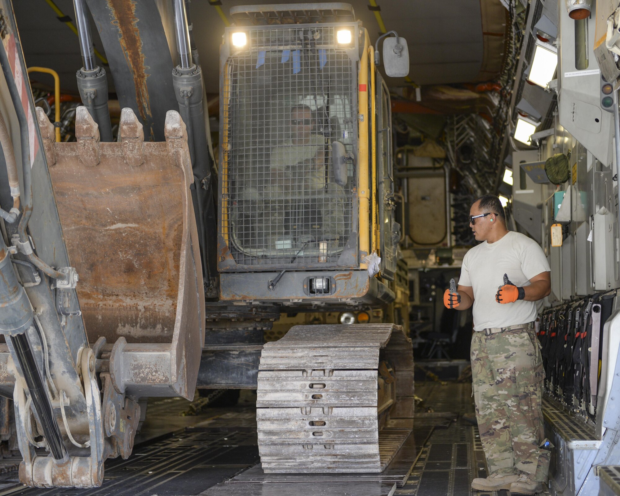 U.S. Air Force Technical Sgt. Alexander Nunez, standing, air transportation/cargo movement team non-commissioned officer in charge, and Staff Sgt. David Wakeman, seated inside the excavator, airfield operator, both assigned to the 557th Expeditionary RED HORSE Squadron, ease an excavator into a C-17 Globemaster III at Al Udeid Air Base, Qatar, Aug. 7, 2017.