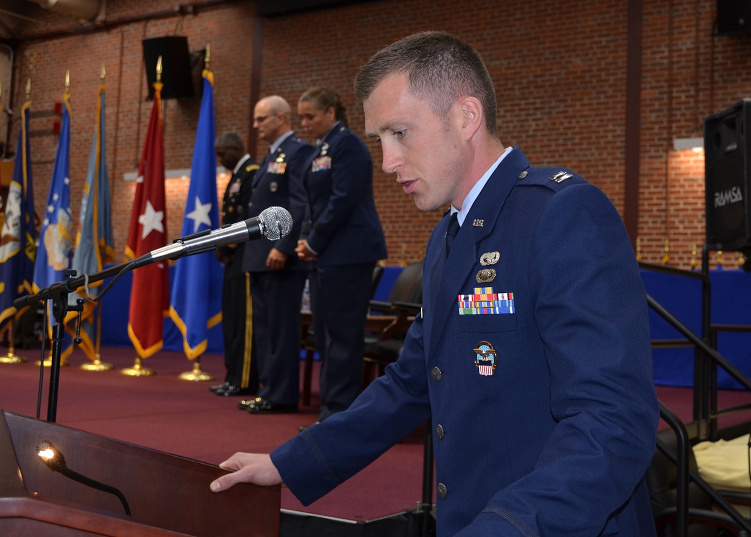 Capt. Musleve stands at a podium and narrates the 2017 DLA Aviation Change of Command Ceremony.