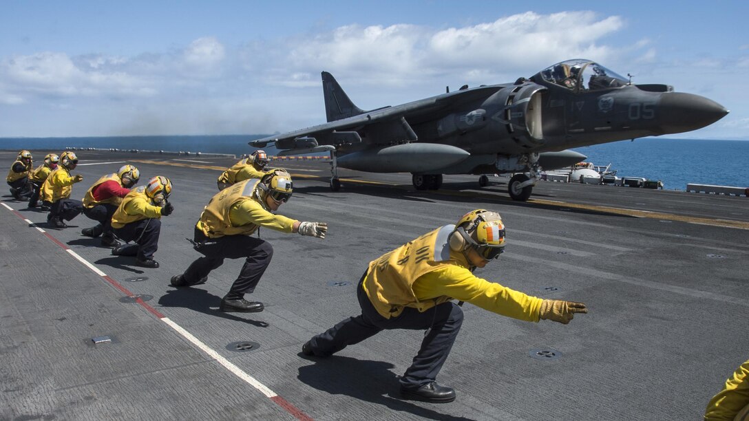 A Marine Harrier aircraft takes off from the flight deck of a ship at sea.