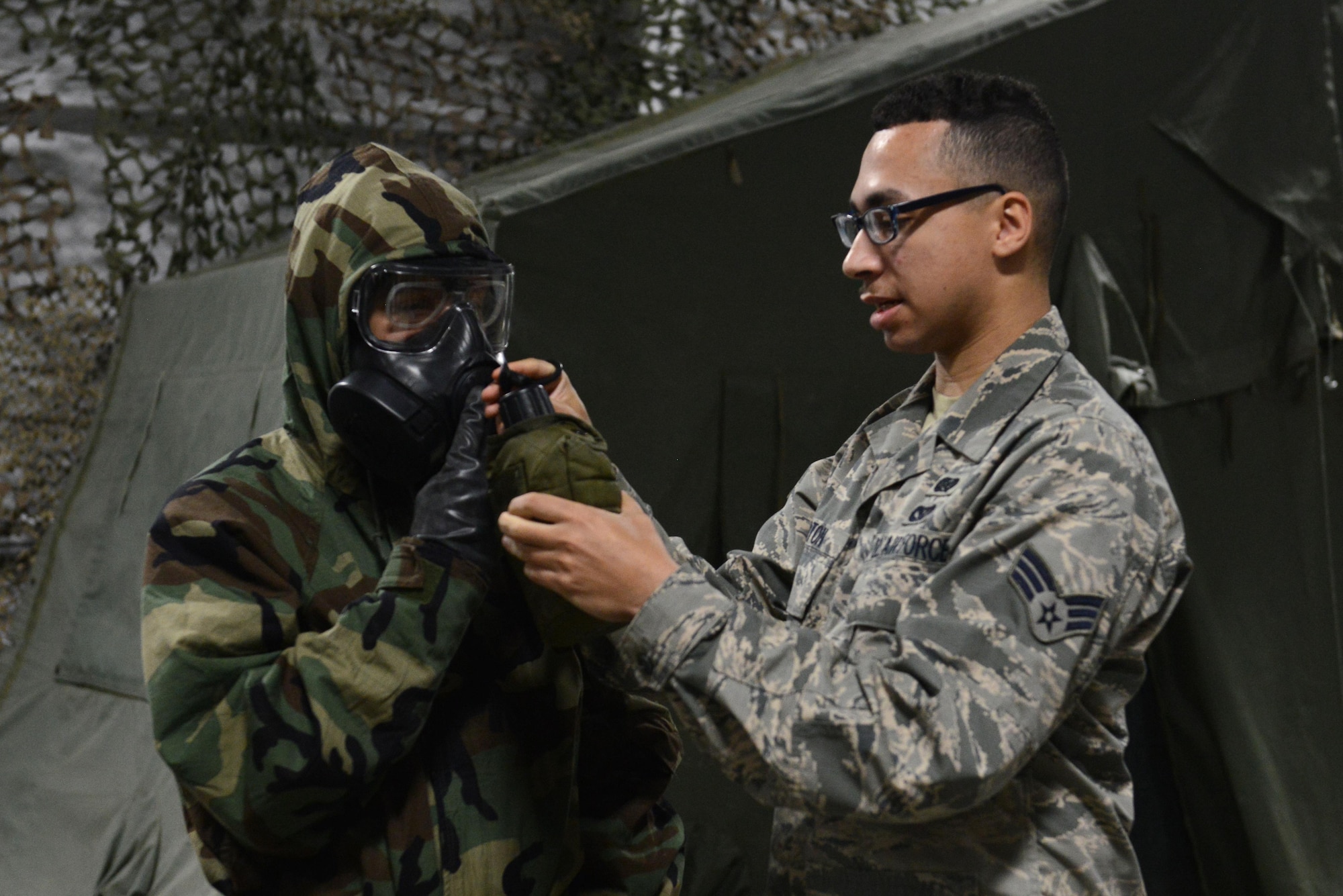Senior Airman Alexander Barton (right), 773d Civil Engineer Squadron emergency management trainer, demonstrates how to drink from a canteen with a gas mask during a Chemical, Biological, Radiological, and Nuclear defense survival skills training class at Joint Base Elmendorf-Richardson, Alaska, Aug. 22. The two-hour CBRN class reminds Airmen of the various equipment and proper procedures used pre- and post-attack, and puts the Airmen’s knowledge to the test with an application of this information in full Mission Oriented Protected Posture gear.