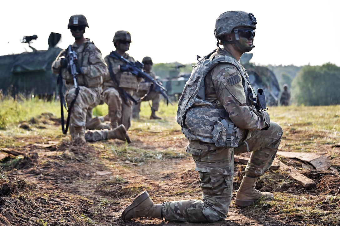 Soldiers take a knee as they provide security in a field during an exercise.