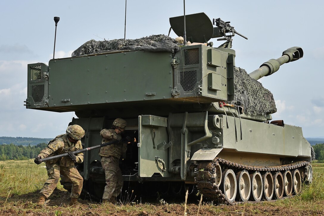 Soldiers prepare an artillery vehicle for an exercise in a field.