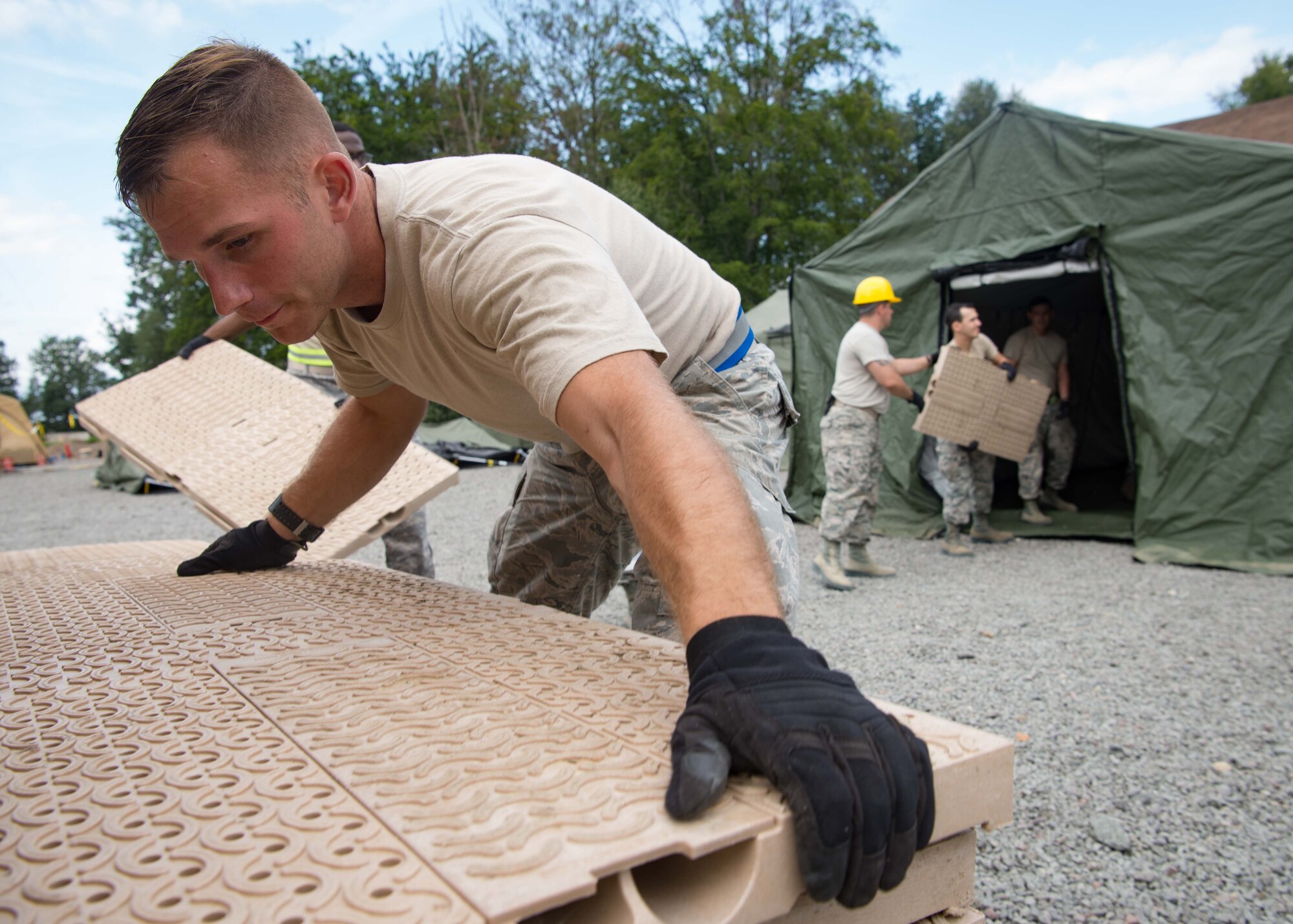 U.S. Air Force Senior Airman Zackery Powers, 1st Combat Communications Squadron radio frequency technician, hands flooring tiles to an assembly line to construct a communications tent during Exercise Lending Hand on Ramstein Air Base, Germany, Aug. 21, 2017.