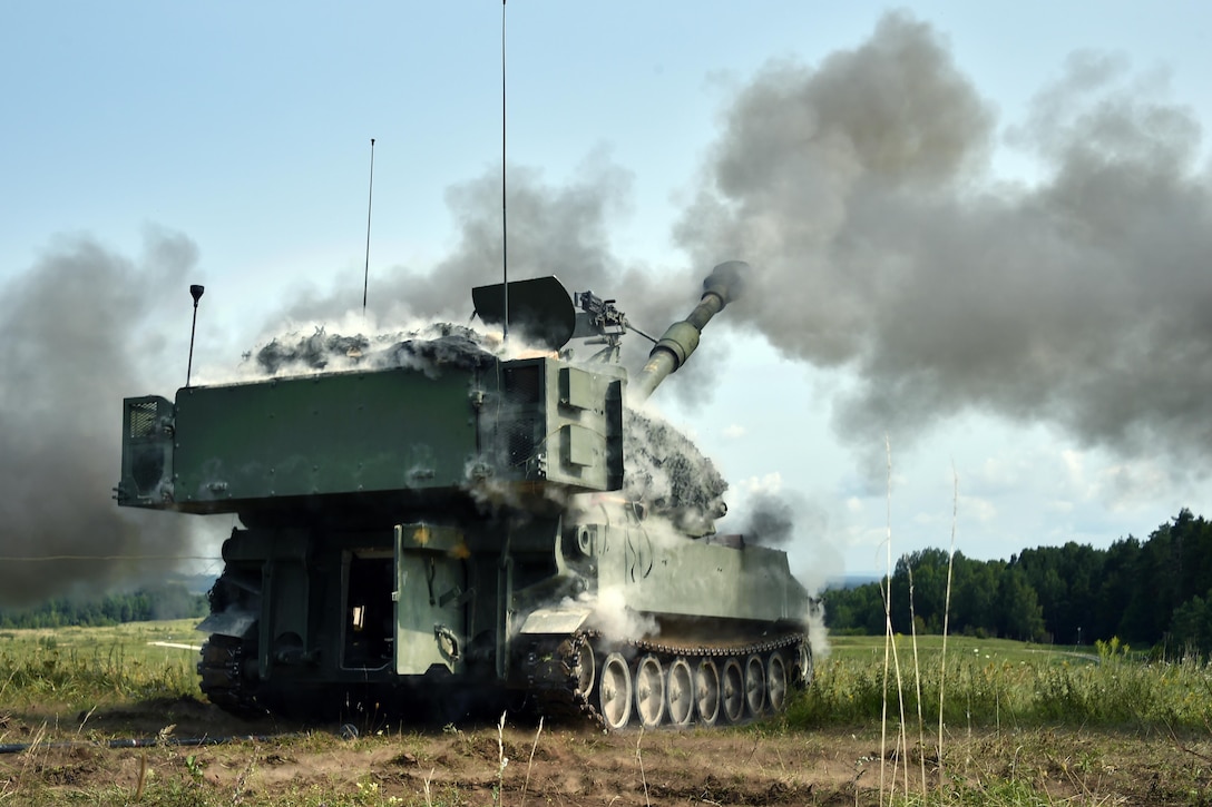 Smoke billows from an artillery vehicle during an exercise in a field.
