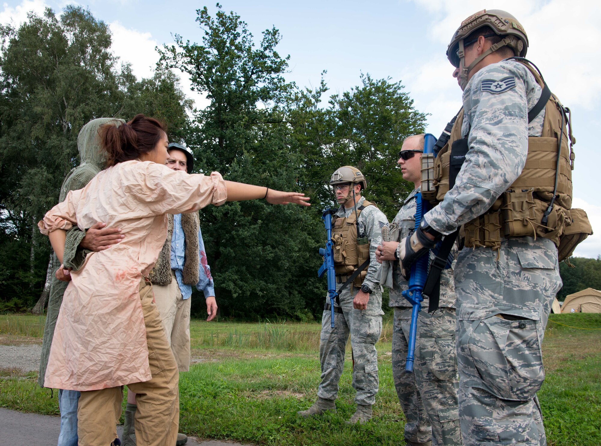 Exercise Lending Hand participants roleplaying as refugees, left, ask U.S. Airmen for water and medical attention during Exercise Lending Hand on Ramstein Air Base, Germany, Aug. 21, 2017.