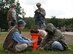 Exercise Lending Hand participants roleplaying as refugees simulate waiting for water and medical care while 435th Security Forces Squadron personnel guard them on Ramstein Air Base, Germany, Aug.