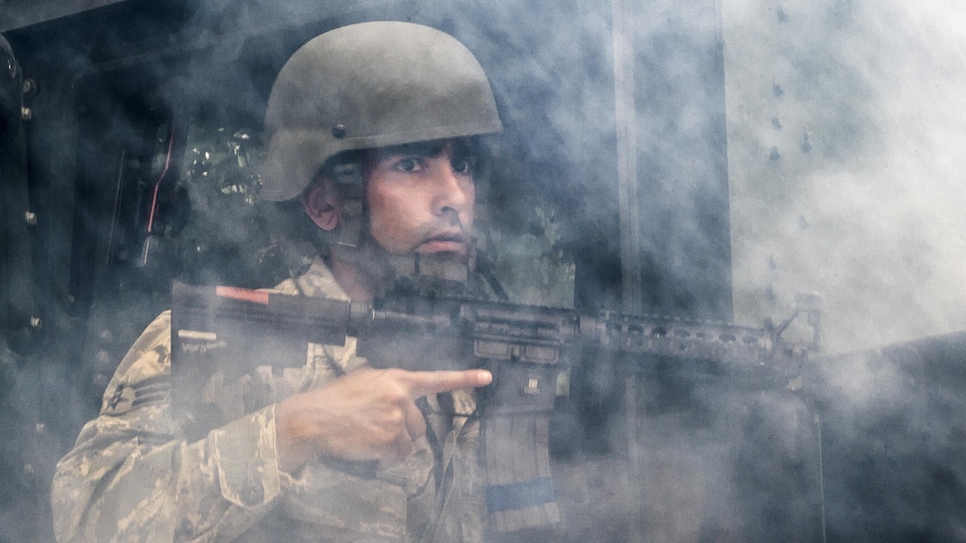 An airmen holding a weapon is surrounded by smoke.