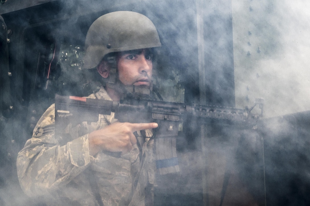 An airmen holding a weapon is surrounded by smoke.