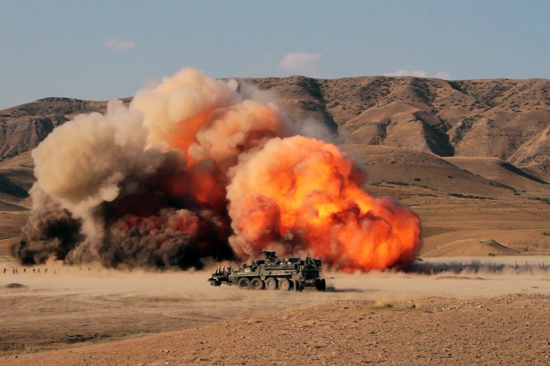 A tank is nearby an explosion with a mountain range in the background.