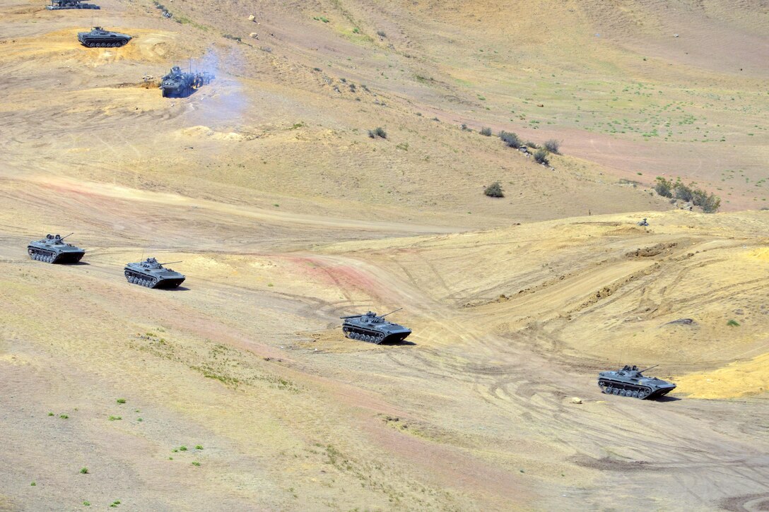 Military vehicles drive though hilly terrain.