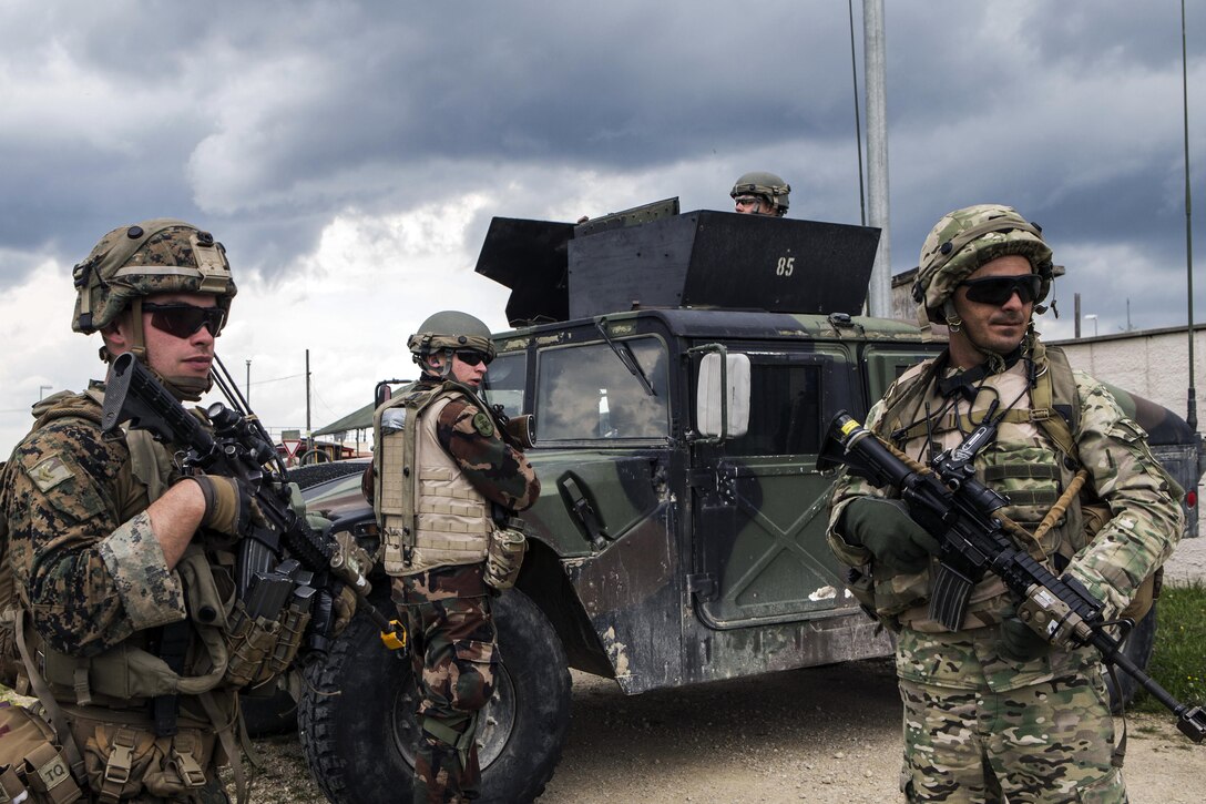 Troops hold weapons and stand by a military vehicle.