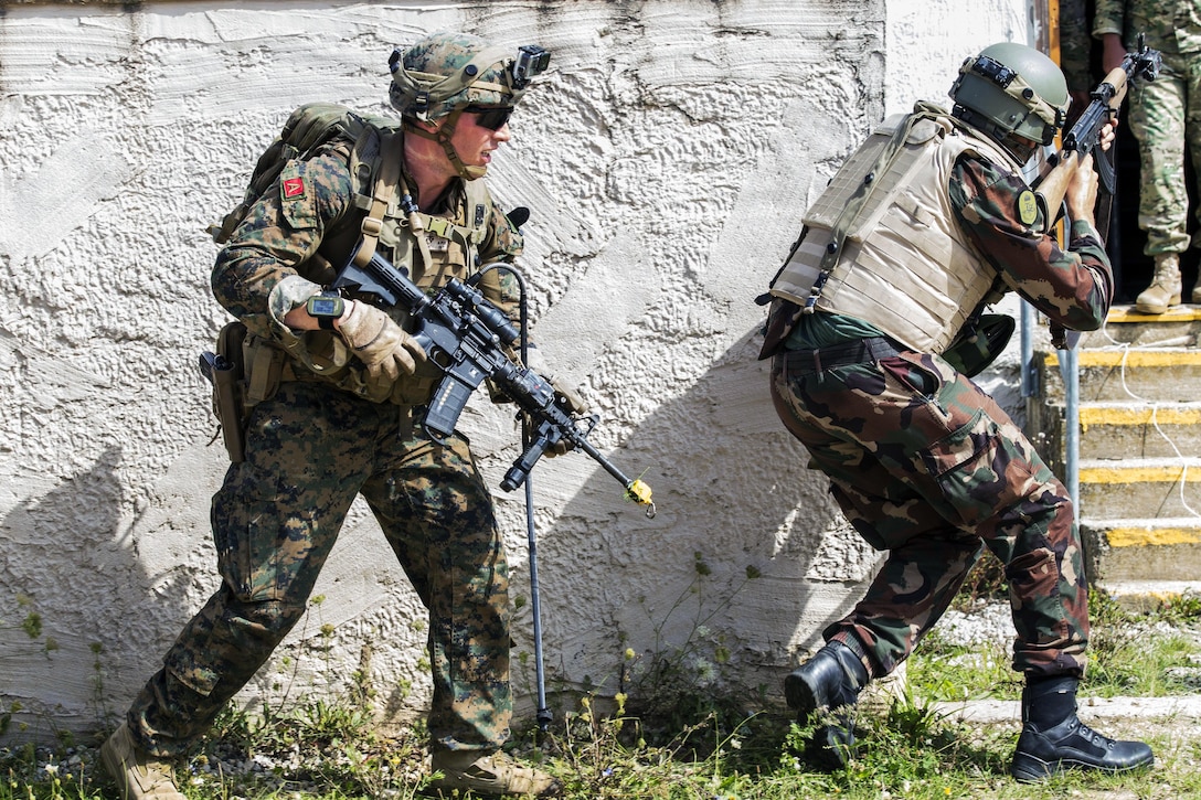Two service members wield message and move along the side of a wall.