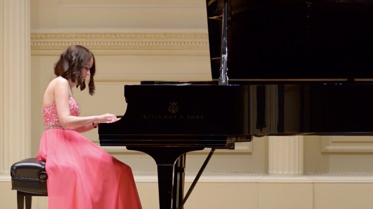 A woman in a coral gown plays piano during a concert.