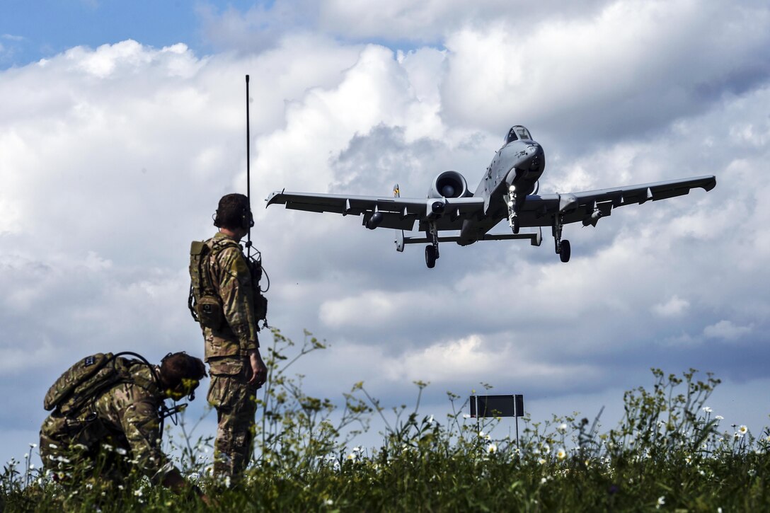Two airmen watch an aircraft in the sky.