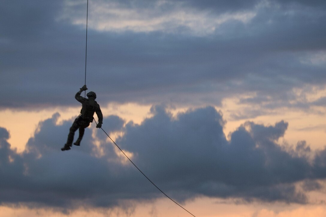 The silhouette of a sailor hangs from a rope against a blue and pink sky.