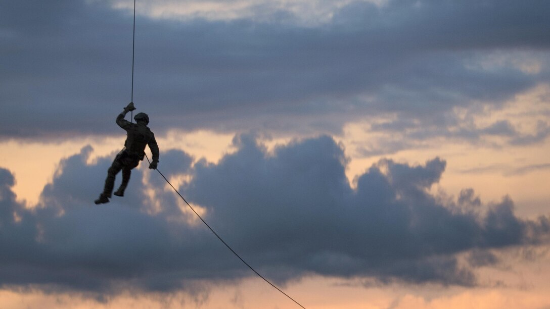 The silhouette of a sailor hangs from a rope against a blue and pink sky.