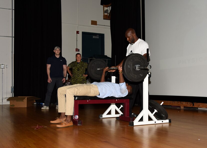 Airman Shemar Ricketts, personnel apprentice with the 319th Force Support Squadron, center, bench-presses 125 pounds as T.J. Tyus, a physical trainer, motivational educator and author, right, spots him during a demonstration at a resiliency conference Aug. 17, 2017, hosted at Canadian Forces Base, Winnipeg, Canada. Tyus was one of four guest speakers, and spoke on the importance of physical resiliency. (U.S. Air Force photo by Airman 1st Class Elora J. Martinez)