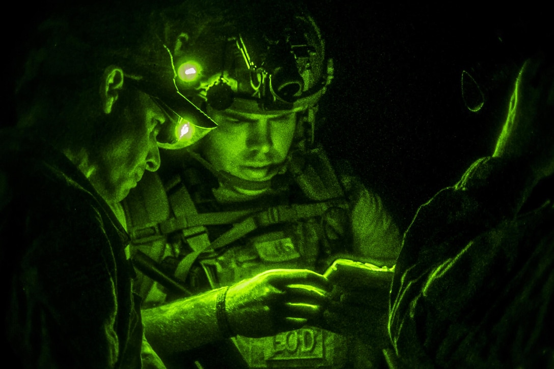 Airmen illuminated by green light huddle together while conversing.