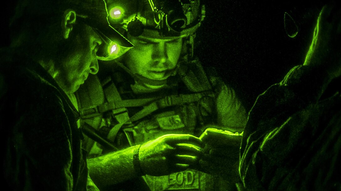 Airmen illuminated by green light huddle together while conversing.