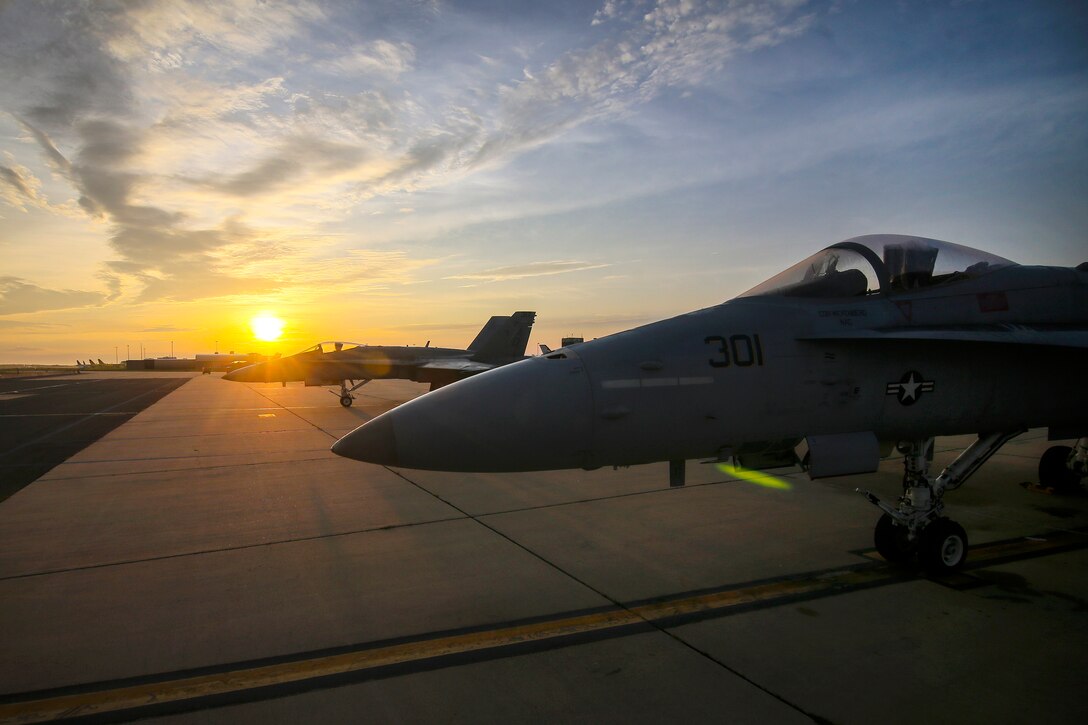 U.S. Navy F/A-18C Hornets sit idle on the flight line at sunrise.