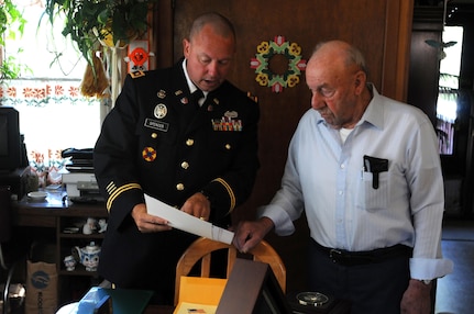 Maj. Christopher Spencer, 88th Regional Support Command retirement services officer, presents Joe Damico with a certificate for one of the awards his brother, Pfc. George G. Damico, earned for his service during the Korean War during a presentation in Cumberland, Wisconsin, August 22. Pfc. Damico was killed in action September 27, 1950 and his remains were never found.