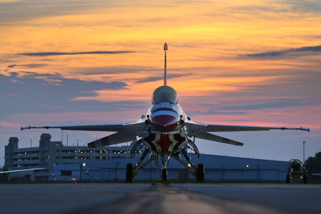 The sun rises behind an F-16 sitting on the flight line