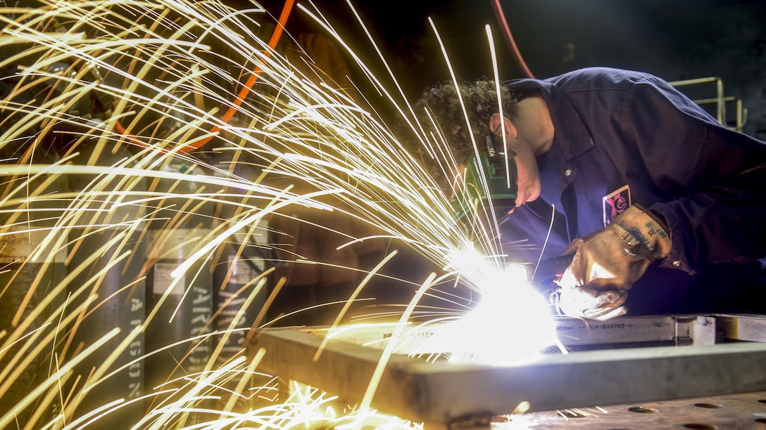 Sparks fly as a sailor wearing protective goggles cuts steel.