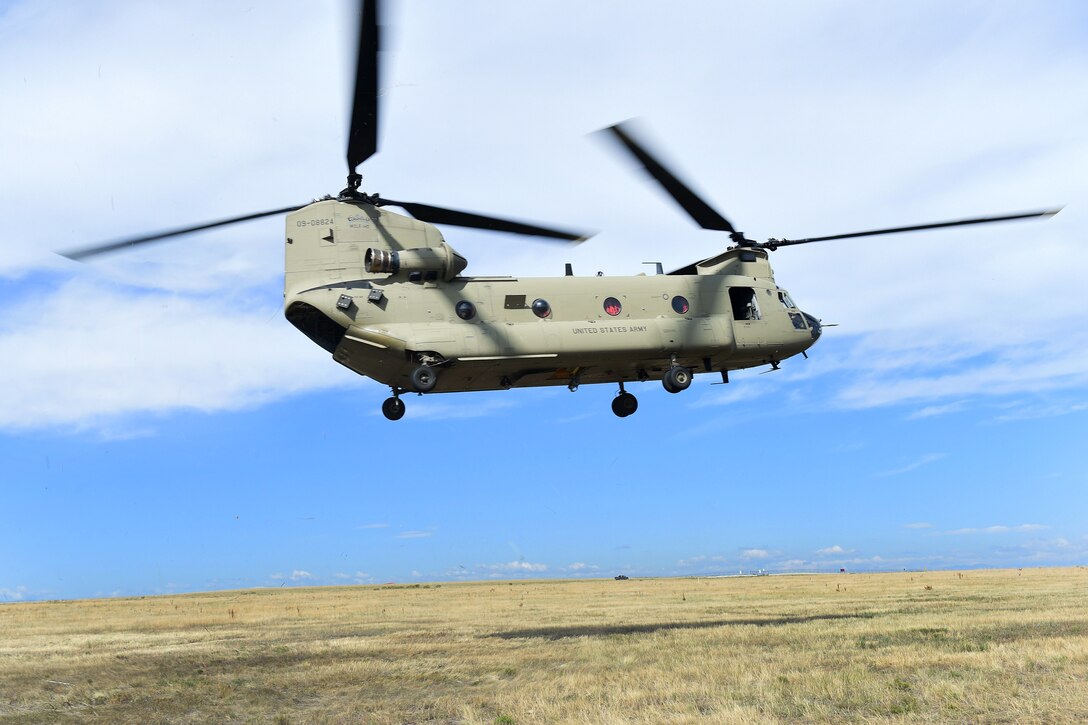 A Chinook helicopter prepares to land in a flat field.