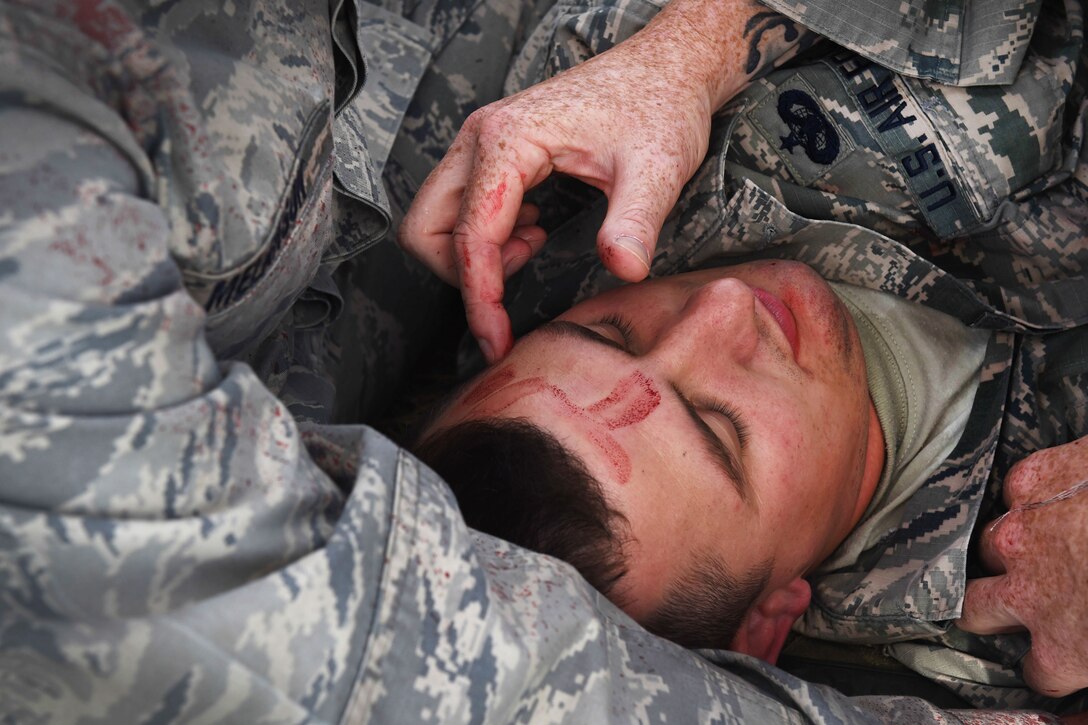 Air Force medical personnel provide medical aid to an airman lying down.