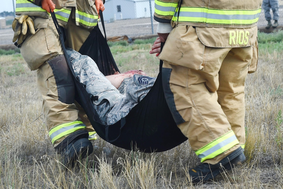 Air Force firefighters move a mock casualty in a flexible stretcher.