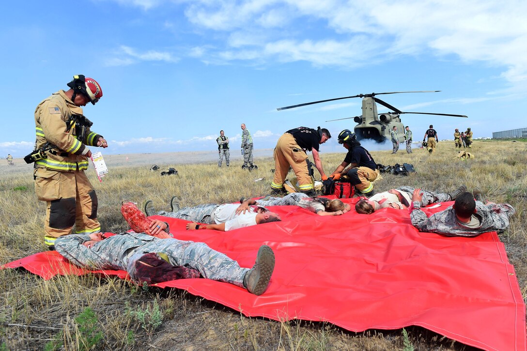 Air Force medical personnel and firefighters provide medical aid to a mock casualties on a red blanket.