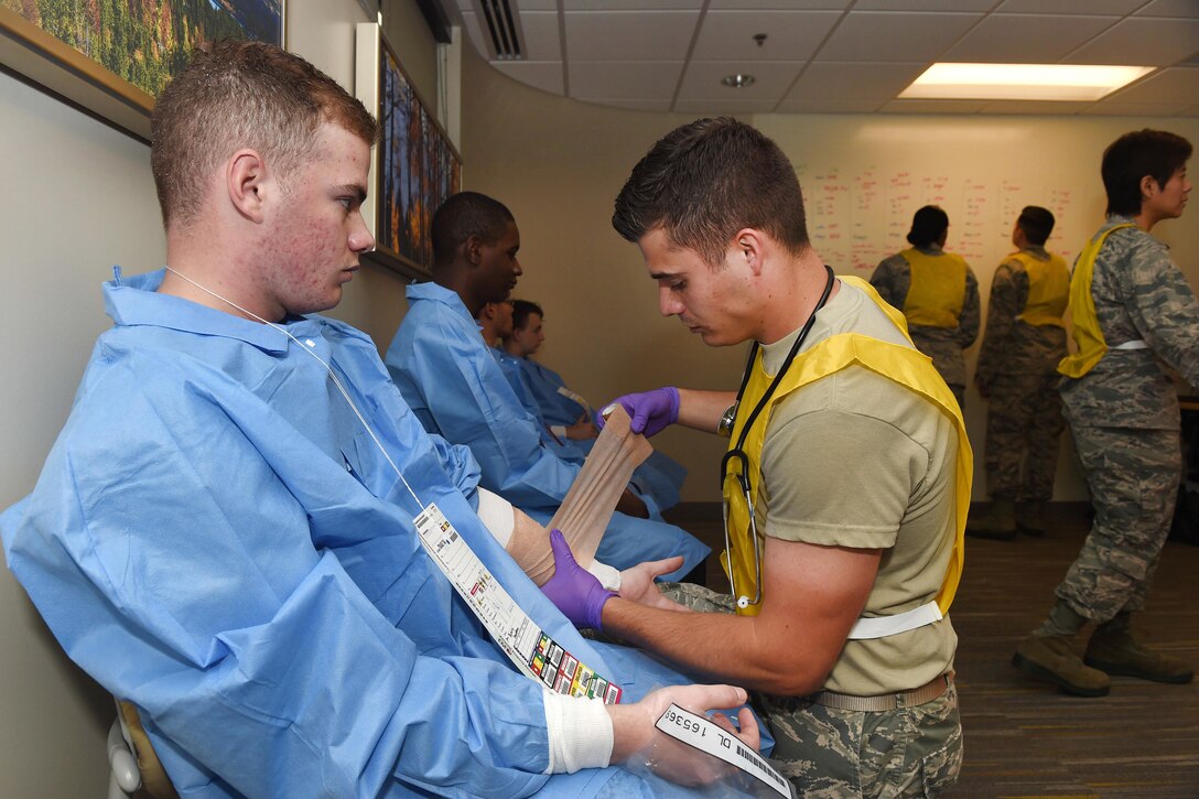 An airman wraps a bandage around the arm of a mock casualty inside a building.