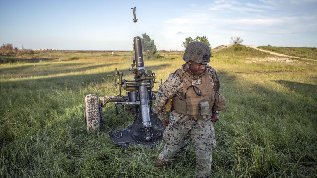 A Marine turns away and clenches his fists as a mortar system fires behind him.