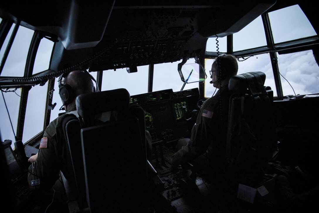Two airmen sit at a cockpit's controls while piloting a plane.